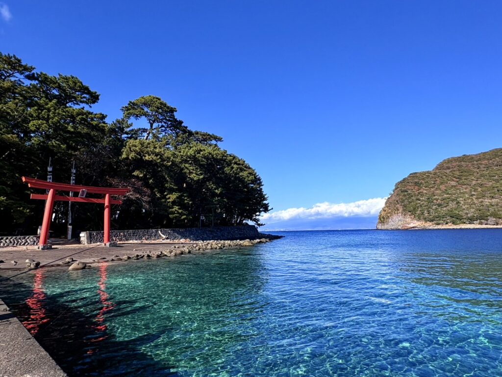 青い空と海に朱色の鳥居、向こうには雲にかかった富士山も見えています。