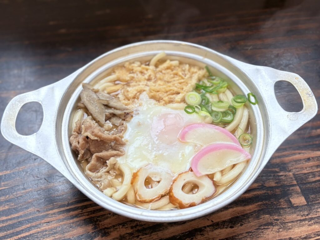 アルミ鍋にうどんと、ちくわ、蒲鉾、ネギ、刻み油揚げ、ごぼう、牛肉。甘めの味の鍋焼きうどんです。