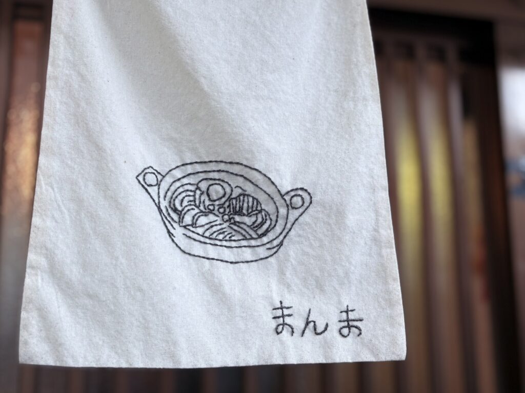 入口のかかっている暖簾が可愛い。鍋焼きうどんの刺繍です。